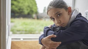 young girl sitting in front of window with hands wrapped around knees