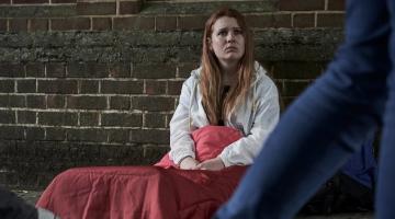 young homeless girl sitting in sleeping bag